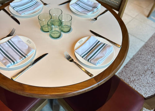 Round dining table set with plates, glasses, and cutlery and bistro napkins in a restaurant setting. 